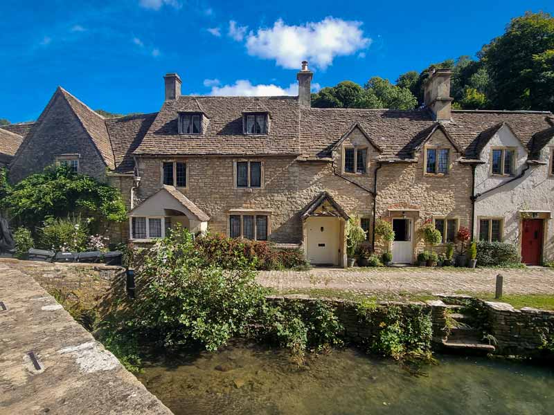 Photo taken on a blue day looking at the golden stone cottages of Castle Combe.