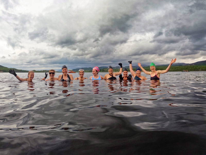 A group of women smile and laugh into the camera while out in a calm lake.