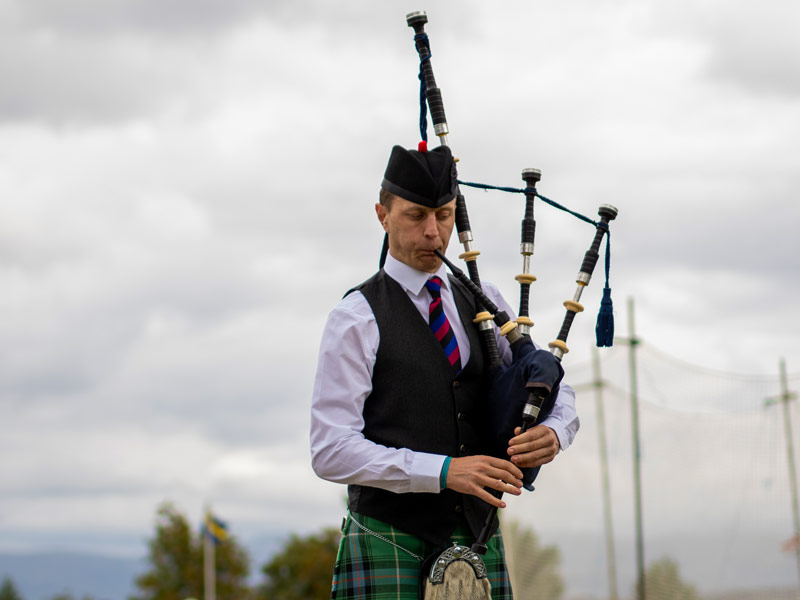 Photo of a piper in costume, facing the camera, playing the bagpipes.