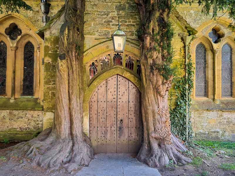 The studded wooden door of St Edwards Church flanked by two trees, said to be the inspiration for the Doors of Durin in The Hobbit.